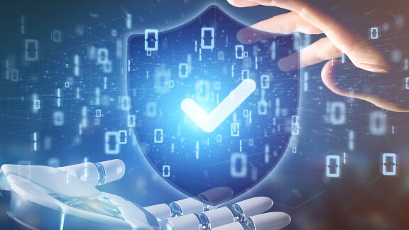 An abstract shield with check mark being held up by a robotic and a human hand, overlaid with a graphic of binary digits